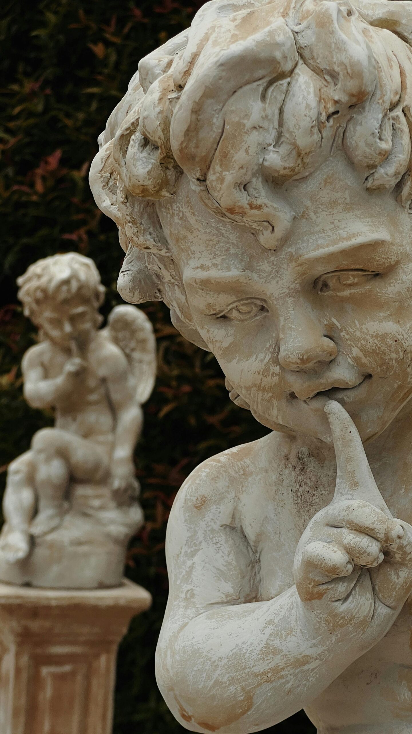 Detailed view of cherub statues depicting shushing gesture in a tranquil garden.