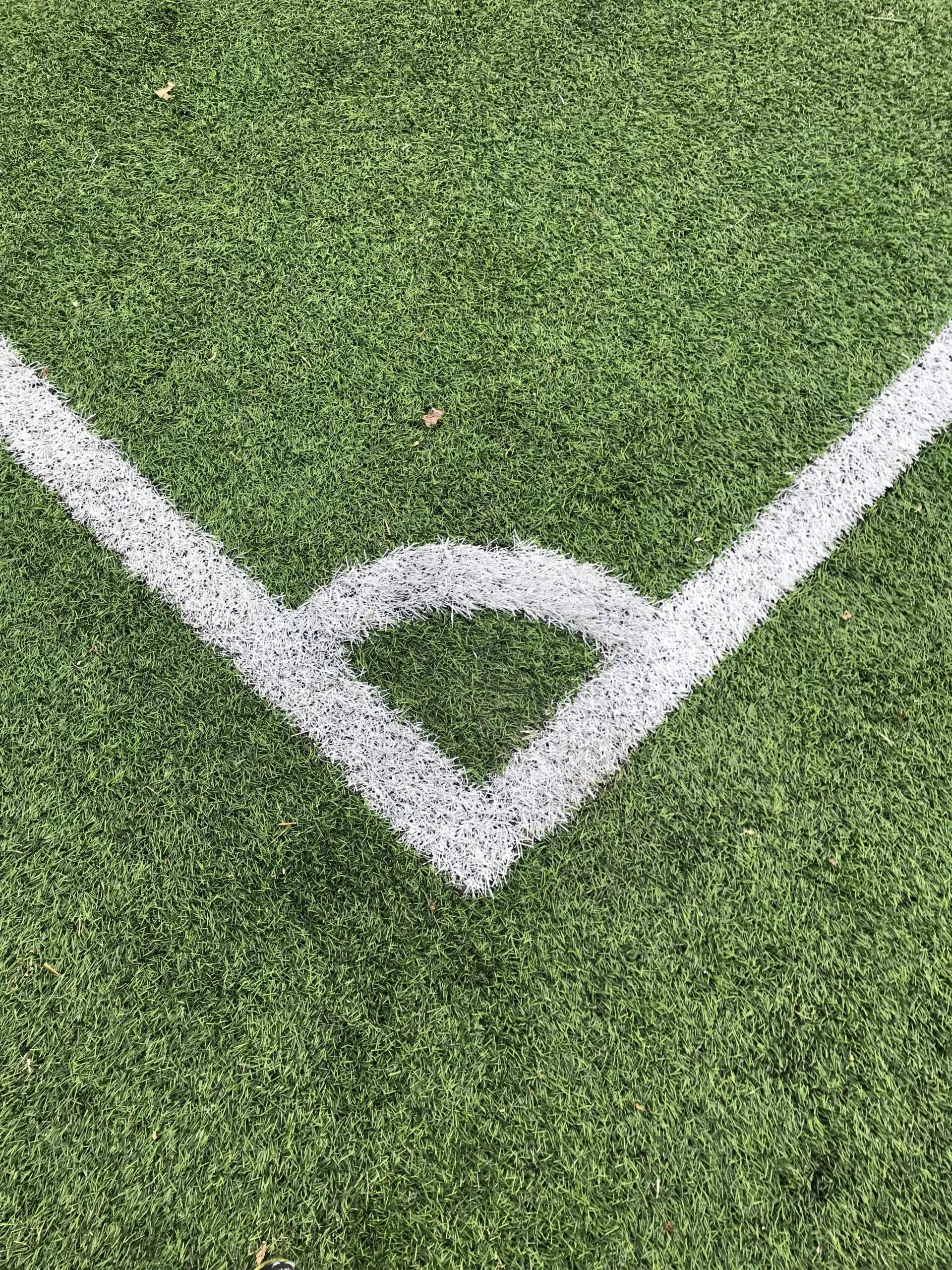 Detailed close-up of a white corner line on a green soccer field turf.