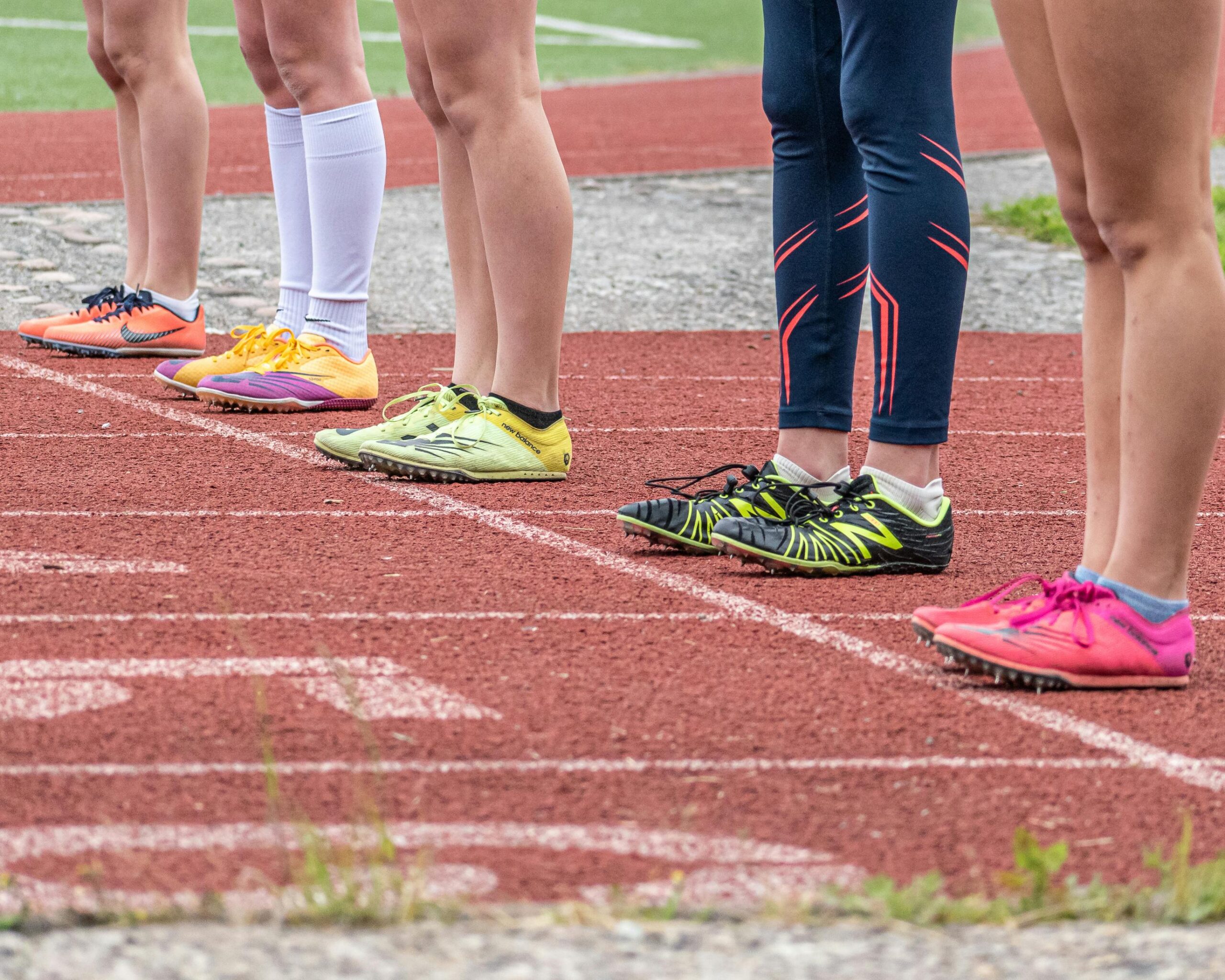 Group of runners preparing to start a race with vibrant footwear on a track.
