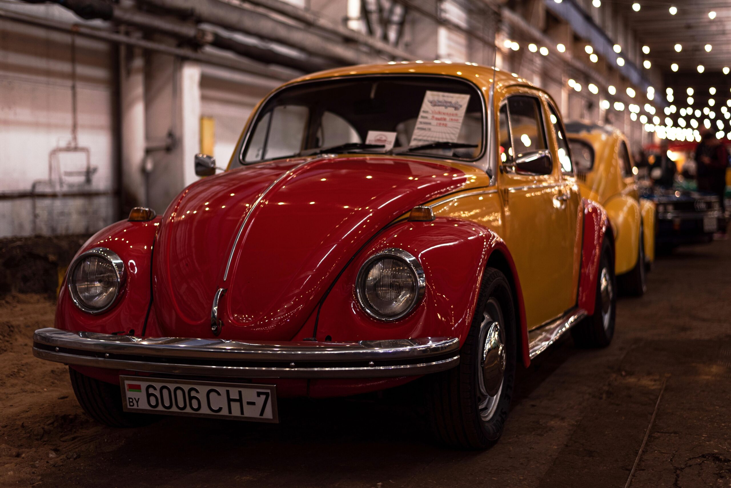 A vintage red and yellow Volkswagen Beetle displayed indoors under string lights.