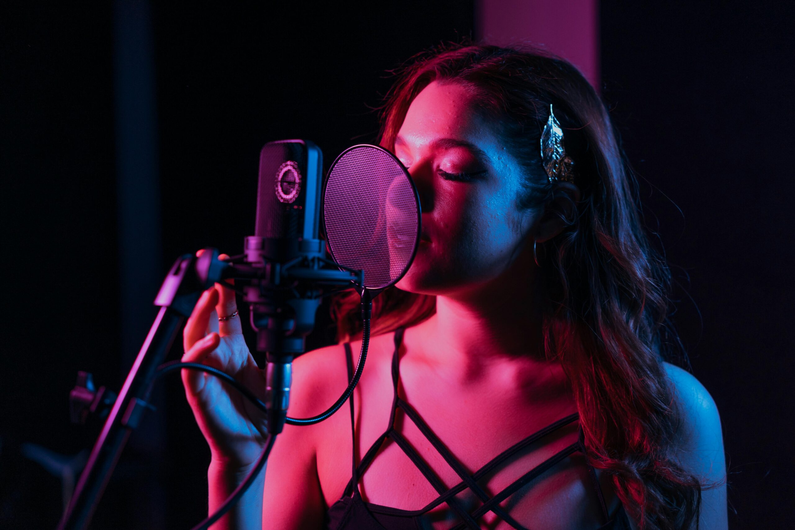 A woman passionately singing into a microphone in a dimly lit recording studio.