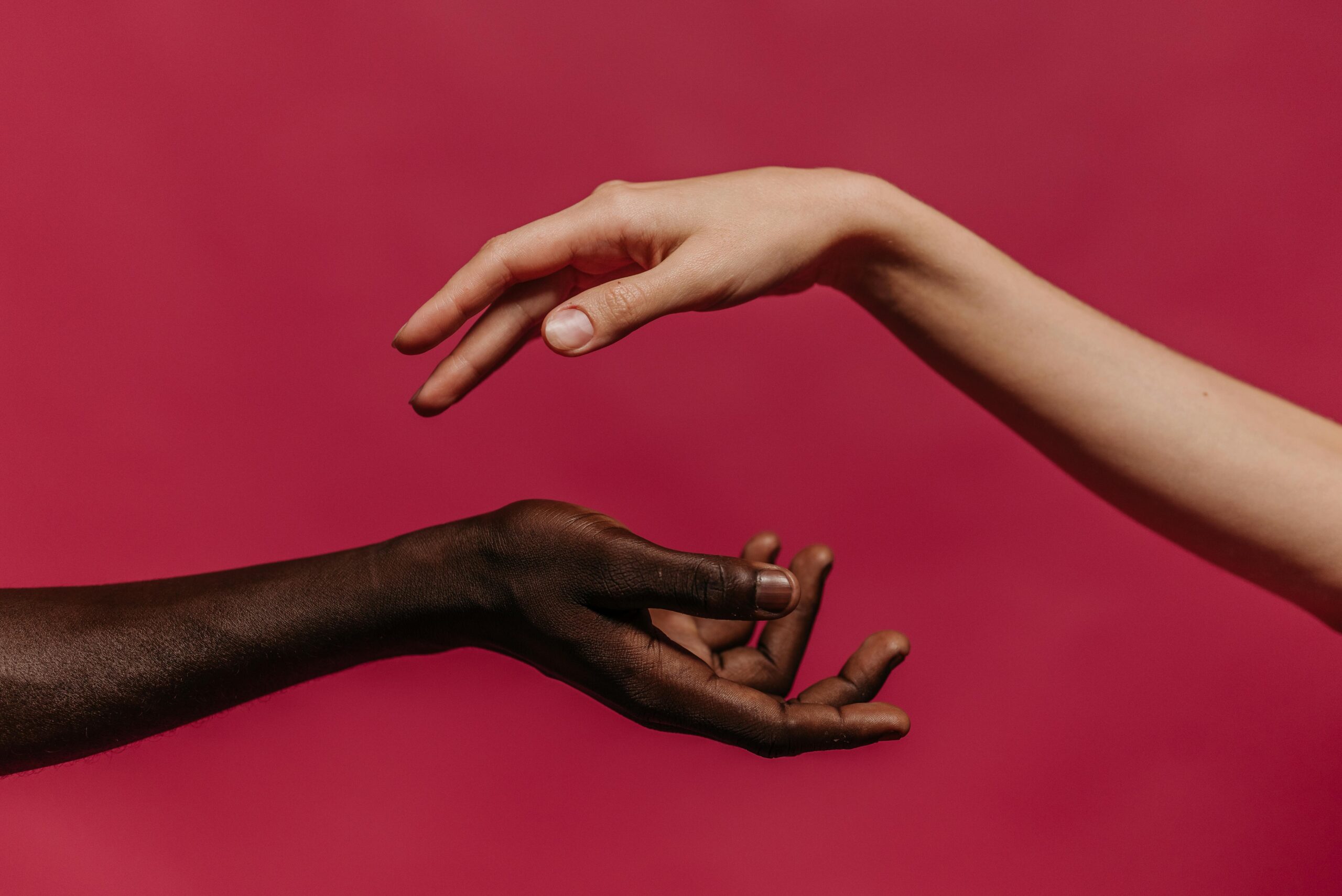 Two hands reaching towards each other against a vibrant pink background, symbolizing connection and diversity.