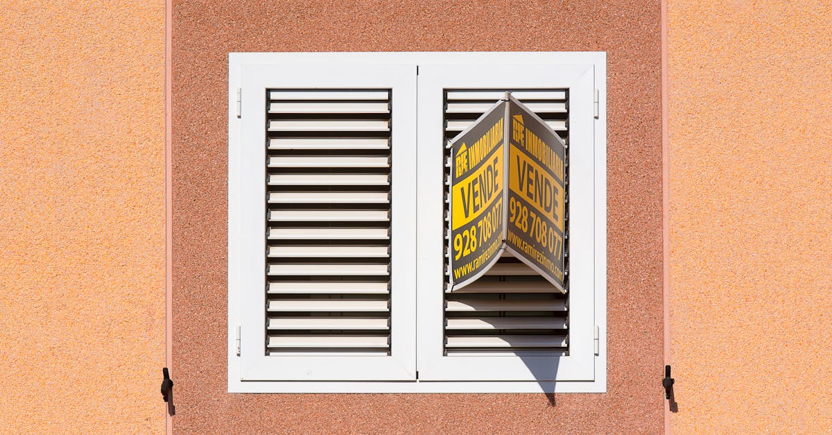White shutter window with a for sale sign on peach building exterior.