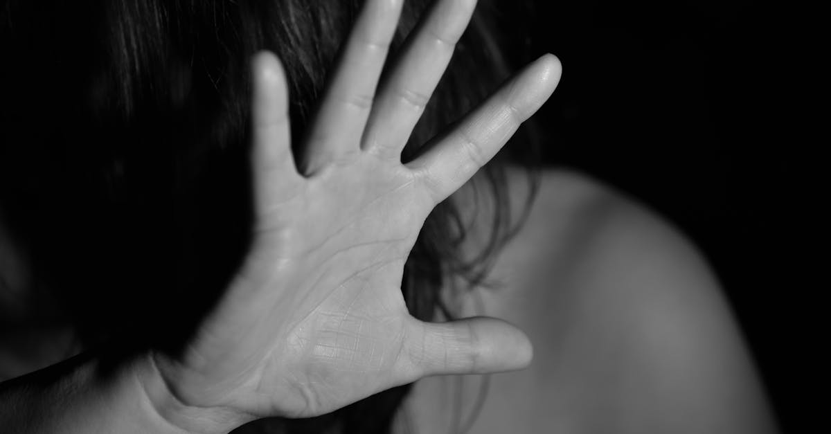 A black and white photo of a woman raising her hand, obscuring her face, suggesting a stop gesture.