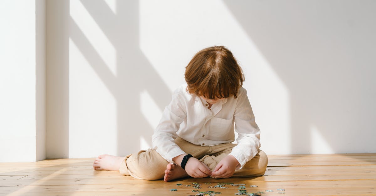 Child sitting on wooden floor concentrating on puzzle pieces, bathed in warm natural light.